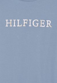 Světle modré bavlněné tričko s bílým nápisem "HILFIGER" s mírně vyvýšenou texturou, umístěným uprostřed přední části. Krátké rukávy, kulatý výstřih.