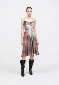 Robe sans manches jusqu'aux genoux avec un imprimé floral brillant dans des tons rouges et verts, complétée par des bottes noires décontractées.