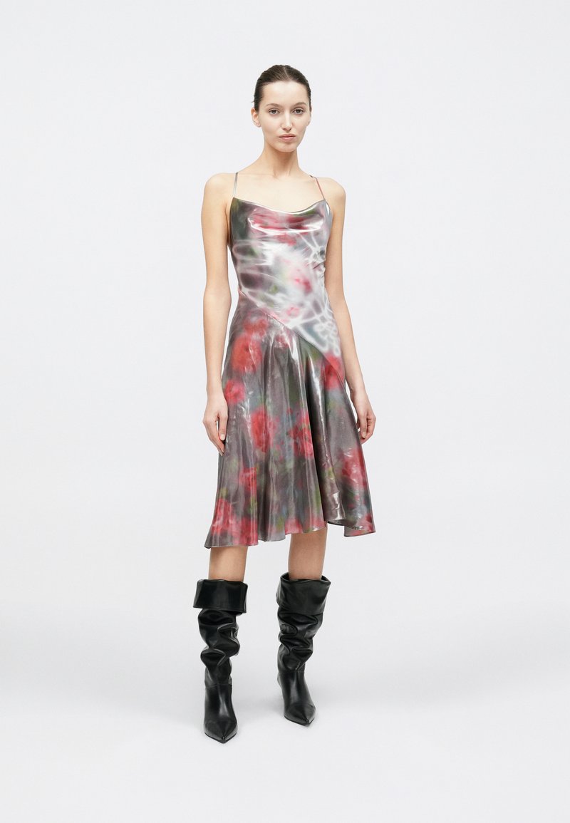 Robe sans manches jusqu'aux genoux avec un imprimé floral brillant dans des tons rouges et verts, complétée par des bottes noires décontractées.