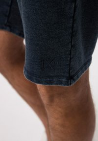 Donkerblauwe shorts van een gestructureerde stof, met een klein, gebossen logo dicht bij de zoom. Het ontwerp heeft een relaxed fit en is kniehoog.