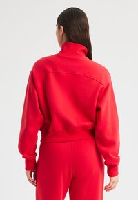 Sweatshirt rosso cropped con collo alto e maniche lunghe. Realizzato in materiale morbido con una texture liscia e polsini a costine. Dettaglio di cucitura minimale.