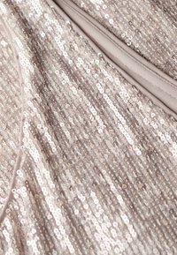 Paillettenstoff in sanftem Beige mit abwechselnd glänzenden und matten runden Pailletten, gesäumt mit einem soliden beigen Rand an einer Kante.