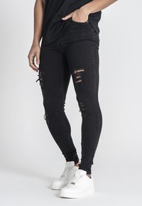 Mustat skinny-farkut, joissa on kuluneita repeämiä, istuvat hyvin ja niissä on hillitty venyvyys. Yhdistetty valkoisiin tennareihin rentoa tyyliä varten.