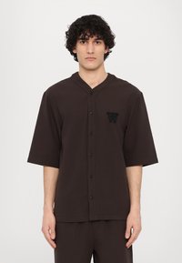 Brown short-sleeve button-up shirt with a v-neck, featuring a textured fabric and an embroidered letter "W" on the left chest.