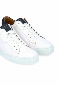 Baskets blanches en cuir avec une semelle en caoutchouc texturé, présentant un accent bleu marine au niveau du talon et une étiquette de langue marquée. Lacets et col rembourré.