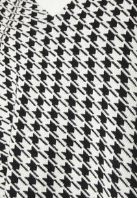 Pull en tricot noir et blanc présentant un motif pied-de-poule avec un col en V. Tissu texturé et formes géométriques distinctes.