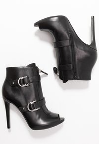 Czarne skórzane botki na wysokim obcasie z odkrytymi palcami, srebrnymi klamrami i suwakiem po boku. Gładka faktura.