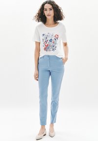Camiseta blanca con estampado floral en azul y rojo, combinada con pantalones de mezclilla de color azul claro y bailarinas beige. Tela suave con un corte relajado.