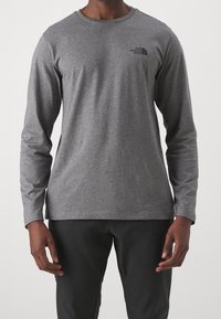 Langärmliges graues T-Shirt aus weichem Stoff, mit Rundhalsausschnitt und einem kleinen schwarzen Logo auf der oberen linken Brust.