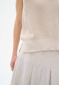 Beige stickad linne med ribbat fåll, i kombination med en ljusgrå veckad kjol i strukturtyg. Fokusera på textur och färgkontrast.