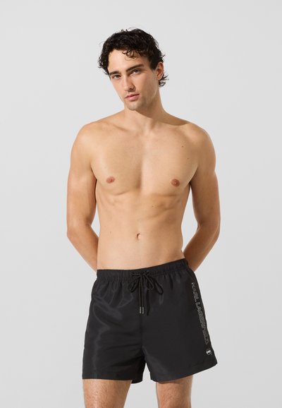 Shorts de bain noirs en tissu léger avec une taille élastique et un cordon de serrage. Détail du logo sur le côté. Design lisse et simple.