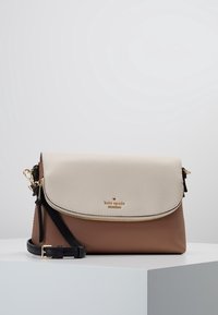 Leather crossbody bag in cream and brown with gold hardware, zip closure, and adjustable black strap. Smooth and textured surfaces.