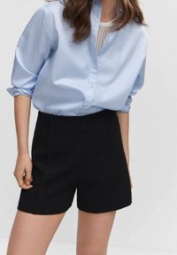Jasnoniebieska koszula na guziki z podwiniętymi rękawami, w połączeniu z czarnymi szortami z wysokim stanem. Gładki materiał, dopasowany krój i minimalistyczne detale.