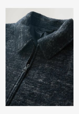 Ciemnoszara wełniana kurtka z teksturowanej tkaniny, z wysokim kołnierzem i widocznym czarnym zamkiem błyskawicznym częściowo zapiętym.
