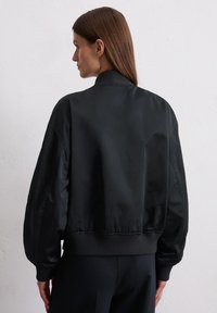 Black bomber jacket in sleek, matte fabric with a ribbed collar and cuffs; features relaxed, oversized fit and simple design.