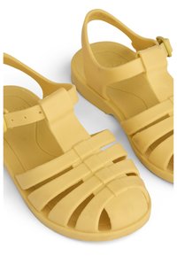 Κίτρινα λαστιχένια σανδάλια με ανοιχτή μύτη, περαστές λωρίδες που διασταυρώνονται, ρυθμιζόμενο λουράκι στον αστράγαλο και υφασμένο εσωτερικό πάτο για άνεση.