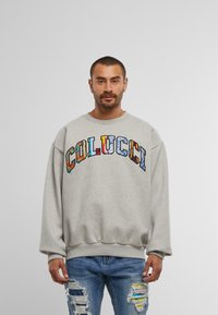Hanorac gri cu un croi supradimensionat, având logo-ul multicolor "COLUCCI" pe piept, cu mansete și tiv cu nervuri. Purtați cu blugi blue jeans uzati.