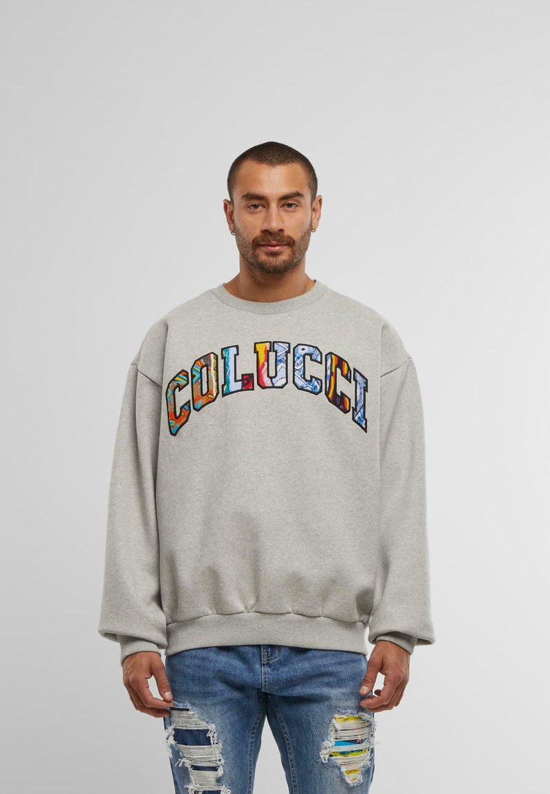 Hanorac gri cu un croi supradimensionat, având logo-ul multicolor "COLUCCI" pe piept, cu mansete și tiv cu nervuri. Purtați cu blugi blue jeans uzati.