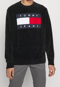 Pull en maille noire avec un logo rectangulaire Tommy Jeans en bleu marine, blanc et rouge sur le devant. Bords-côtes aux poignets et à l'ourlet ; col rond.