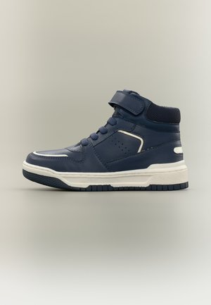 Basket montante bleu marine avec semelle blanche, lacets à l'avant et bande velcro sur col rembourré autour de la cheville sur fond neutre.