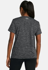 Pilkas, trumpomis rankovėmis sportinis marškinėliai su tekstūruotu dizainu ir logotipu ant nugaros. Pagaminti iš drėgmę sugeriančio audinio.