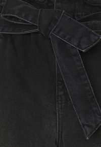Pantalons en denim noir avec une finition texturée, dotés d'une ceinture nouée à la taille et de détails de couture visibles.