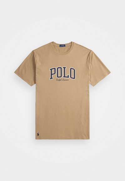 Bež majica kratkih rukava s tekstom "POLO Ralph Lauren" u mornarsko plavoj i bijeloj boji na prsima, malo logoa igrača polo blizu donjeg rubа.
