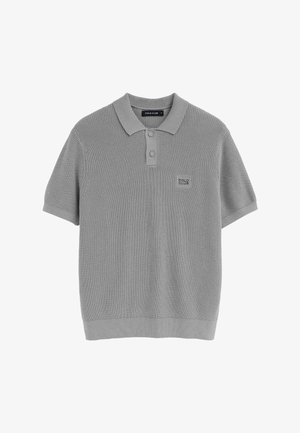 Polo de punto de manga corta color gris claro con dos botones forrados de tela y un pequeño parche "Polo Club" en el pecho izquierdo.