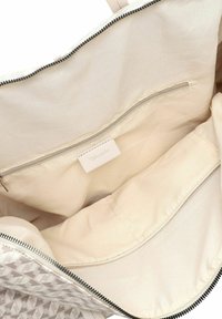 Sac fourre-tout en tissu texturé avec un motif géométrique en gris et blanc. L'intérieur présente une doublure crème et une poche zippée.