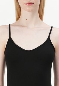 Μαύρο τοπ με λεπτές τιράντες, που διαθέτει V-λαιμόκοψη και λεία υφή. Το υλικό φαίνεται να είναι ελαστικό και εφαρμοστό.