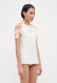 Women's short-sleeve rash guard in white, featuring orange floral patterns on sleeves, and "Ripcurl" logo on the front. Smooth, stretchy fabric.