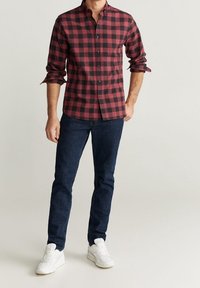 Chemise à carreaux rouges et noirs, à boutons, manches longues, associée à un jean bleu foncé et des baskets blanches. Look décontracté avec une coupe structurée.