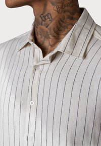 Hemd mit Kragen aus leichtem, strukturiertem Stoff mit vertikalen schwarz-weißen Streifen. Verfügt über weiße Knöpfe entlang der Vorderseite.