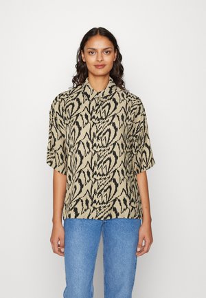 Camicia a maniche corte con bottoni color beige con motivo astratto nero. Presenta un colletto e una vestibilità ampia, realizzata in tessuto morbido. Abbinata a jeans blu.