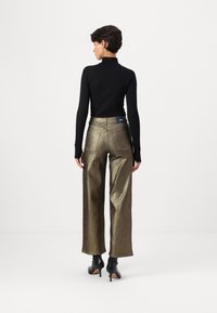 Top negro de mangas largas combinado con pantalones anchos de cintura alta en metálico dorado. Los detalles incluyen dos bolsillos traseros y una etiqueta de marca en la cinturilla.
