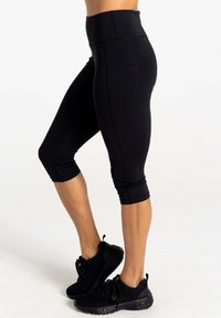 Schwarze Capri-Leggings mit hoher Taille, ausgestattet mit einer glatten Textur, seitlichen Taschen und einem enganliegenden Design, das sich an der Wade verjüngt.