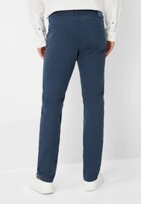 Navyblaue Baumwollhosen mit slim fit, ausgestattet mit zwei Gesäßtaschen und einer glatten Textur, kombiniert mit weißen Sneakers.