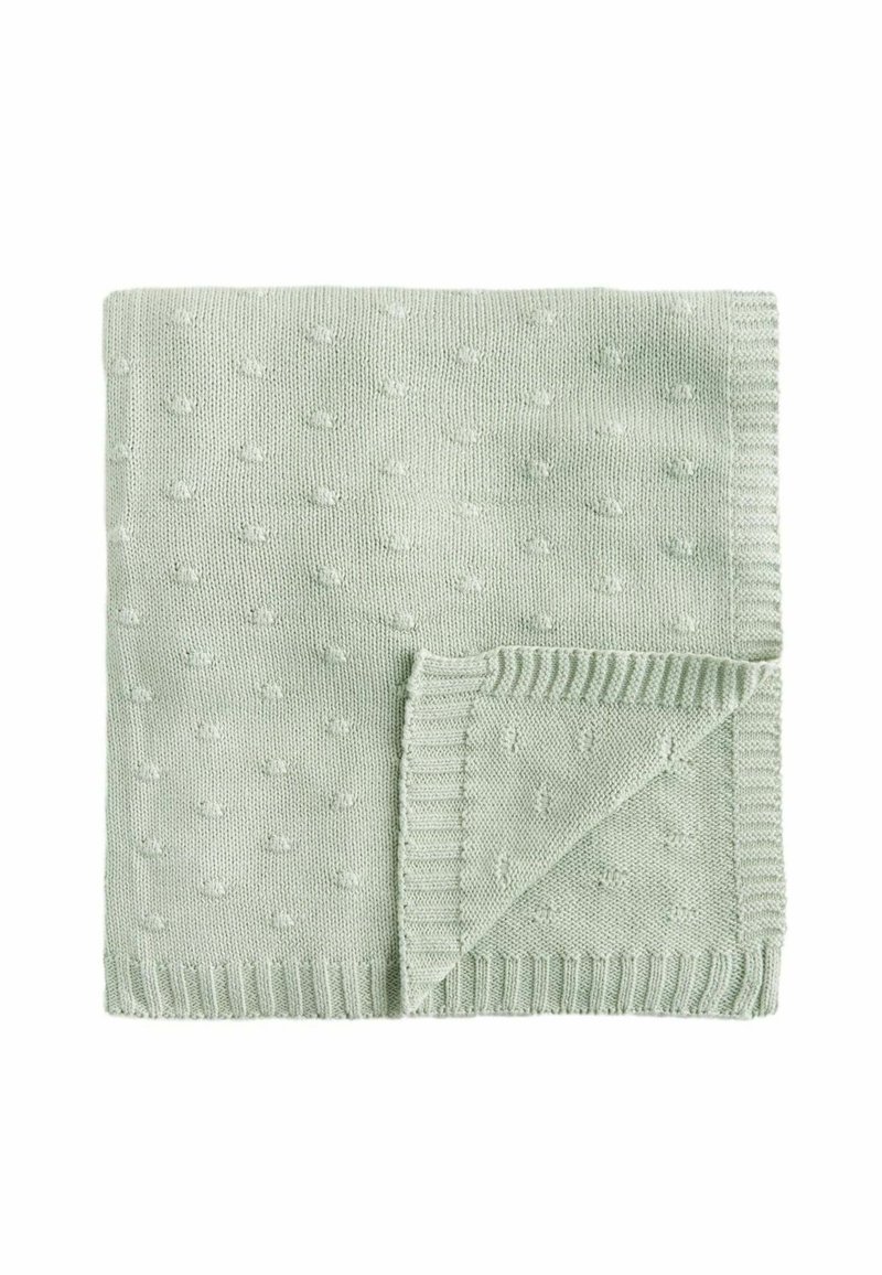 Couverture en tricot vert clair avec un motif de points texturé, présentant des bords côtelés et un coin replié pour plus de détails.