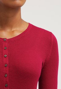 Frambozenkleurige ribgebreide cardigan met een ronde halslijn, sluiting met zwarte knopen aan de voorkant en lange mouwen.