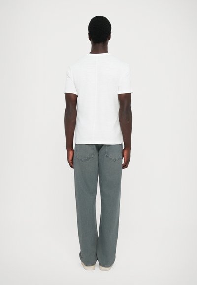White short-sleeve t-shirt made of lightweight fabric, paired with loose-fitting, gray denim pants featuring rear pockets and a straight leg.