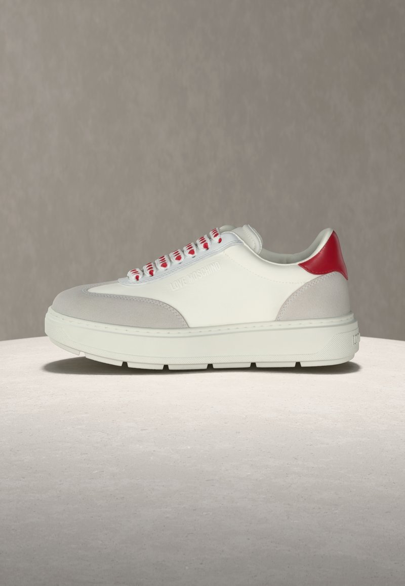Λευκό sneaker χαμηλού τύπου με γκρι σουέντ λεπ τομέρειες, κόκκινη γλώσσα στη φτέρνα, λευκά κορδόνια με κόκκινες λεπτομέρειες και ανάγλυφο το λογότυπο "Love Moschino" στο πλάι.