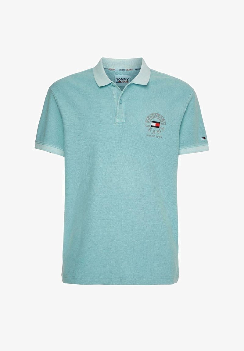 Polo shirt bleu clair à manches courtes avec col, plastron à deux boutons, et patch logo Tommy Jeans sur la poitrine gauche et la manche.