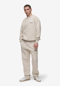 Felpa e pantaloni in cotone beige, con una vestibilità comoda, polsini a costine e logo stampato in nero. Abbinati a sneakers bianche e beige.