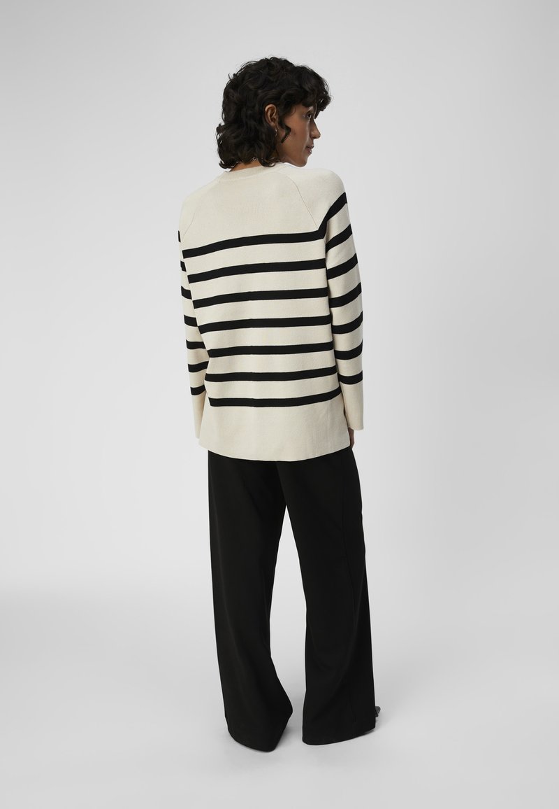 Gestreifter Cremepullover mit schwarzen horizontalen Streifen, lockere Passform, gerippte Textur und überschnittenen Schultern, kombiniert mit schwarzen weiten Hosen.