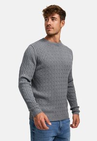 Grå strikkegenser med teksturert mønster, rund hals og lange ermer, kombinert med blå denimjeans.