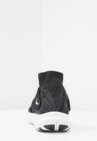Chaussure de sport noire avec un col haut en tricot semblable à une chaussette, un tissu texturé, un logo Nike distinct, et une semelle blanche avec des accents noirs.