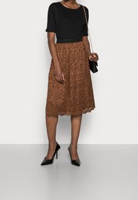 Zwarte geribbelde top met korte mouwen, gecombineerd met een bruine kanten midi rok met intrikate patronen en een gegolfde zoom, gedragen met zwarte stilettohakken.