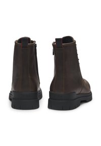 Par de botas cortas de cuero marrón oscuro con suelas gruesas negras, tiradores negros con costuras rojas y cremalleras laterales, vistas desde la parte trasera.
