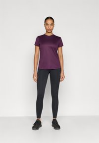 Lilla krohitud t-särk lühikeste varrukatega, ühendatud mustade retuusidega. T-särgil on ümmargune kaelus ja sile pind.