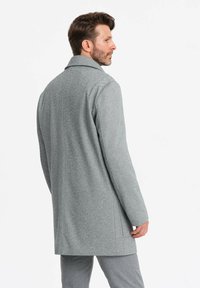 Abrigo de lana gris texturizado con cuello de muesca y corte recto, que presenta un acabado de costura limpio, llevado sobre pantalones gris ajustados.